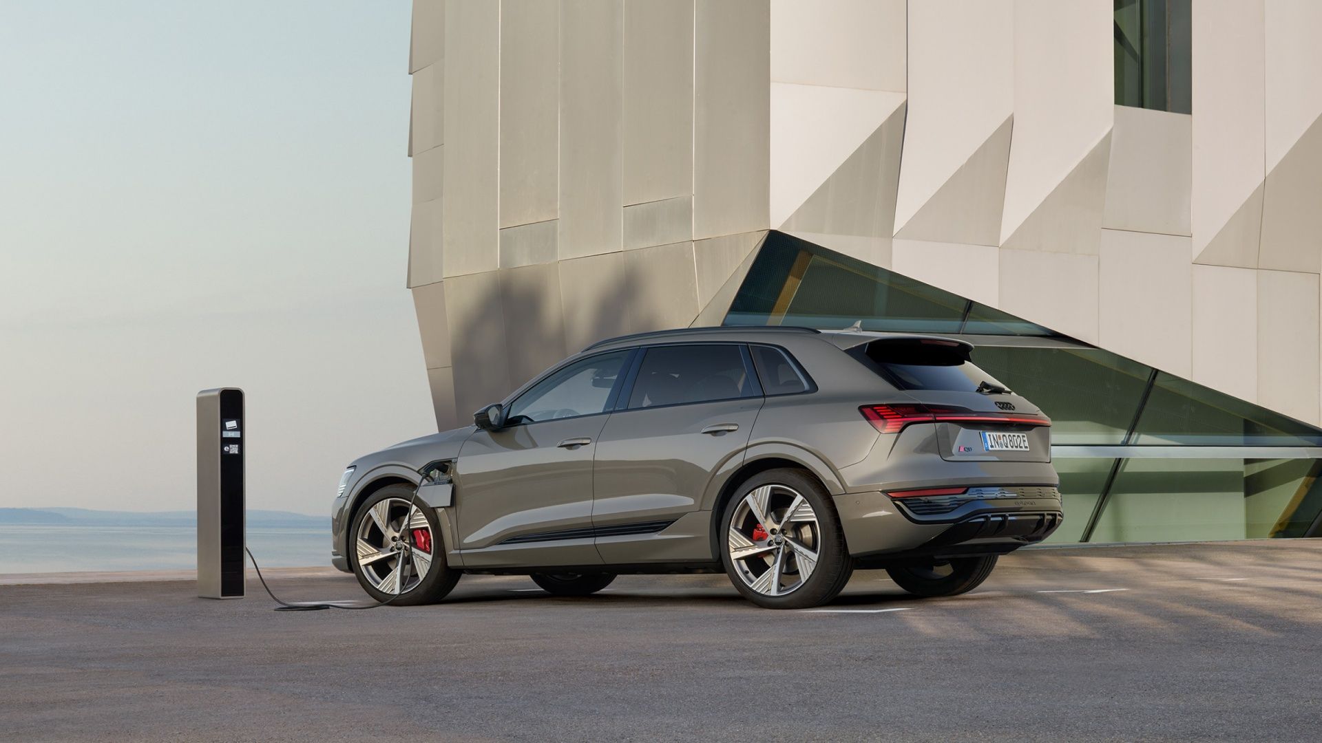 An Audi Q8 e-tron SUV charging in front of a building.
